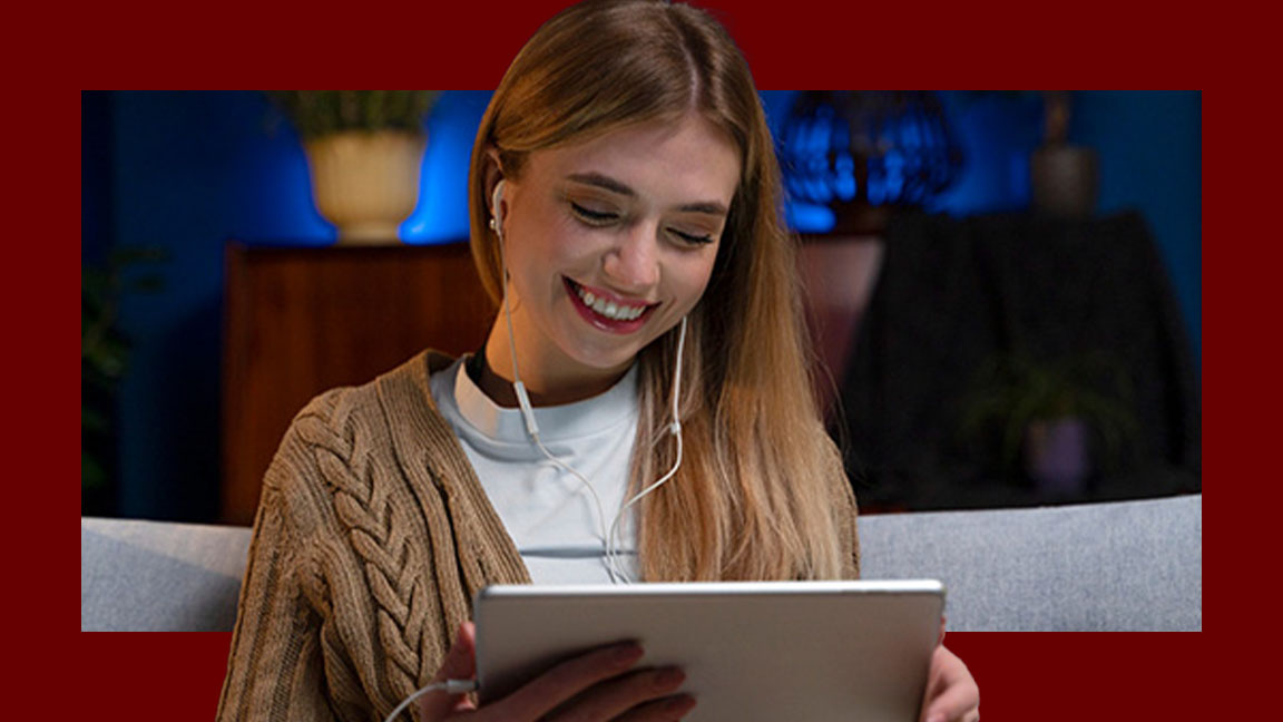 Jovem sorrindo assistindo em tablet e utilizando fone de ouvido